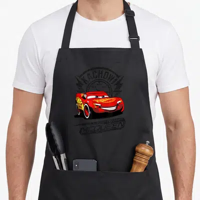 Kachow car apron - Red Lightning McQueen car with KACHOW! speedometer graphic and name below — shown on a black cotton canvas apron against a white background