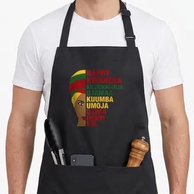 Principle african apron - Woman profile with turban and stacked Kwanzaa principle words in red green yellow brown — shown on a black cotton canvas apron against a white background