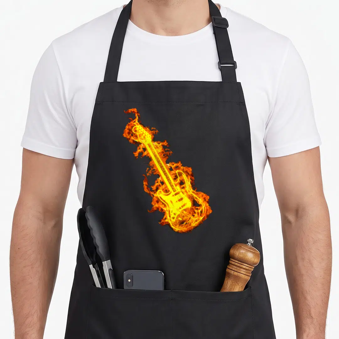 Electric flame apron - Realistic electric guitar engulfed in orange and yellow flames on black fabric — shown on a black cotton canvas apron against a white background