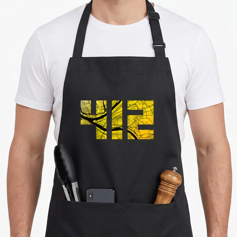 Map pittsburgh apron - 412 number shape filled with yellow and black street map lines — shown on a black cotton canvas apron against a white background
