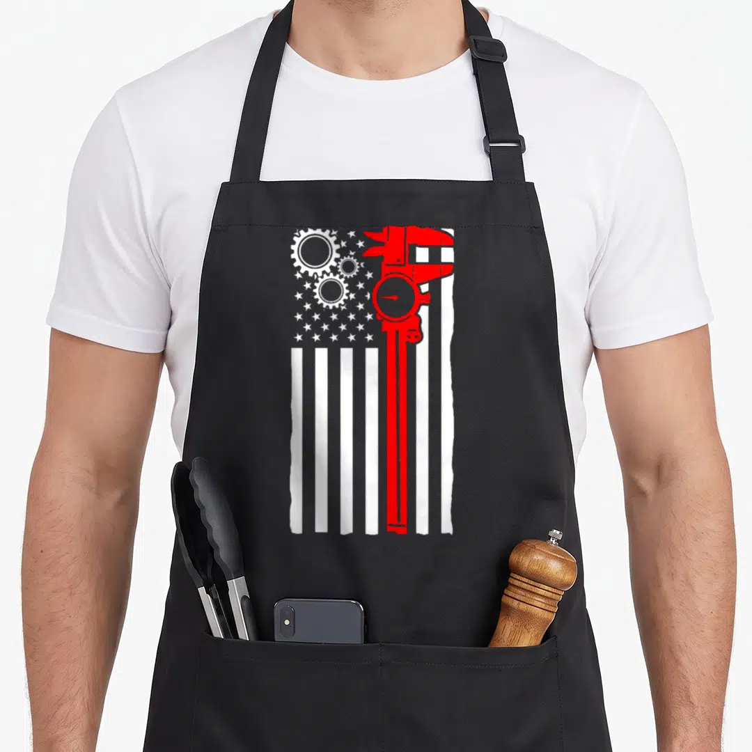 Flag machinist apron - Red caliper and white gears on white flag stripes minimalist design — shown on a black cotton canvas apron against a white background
