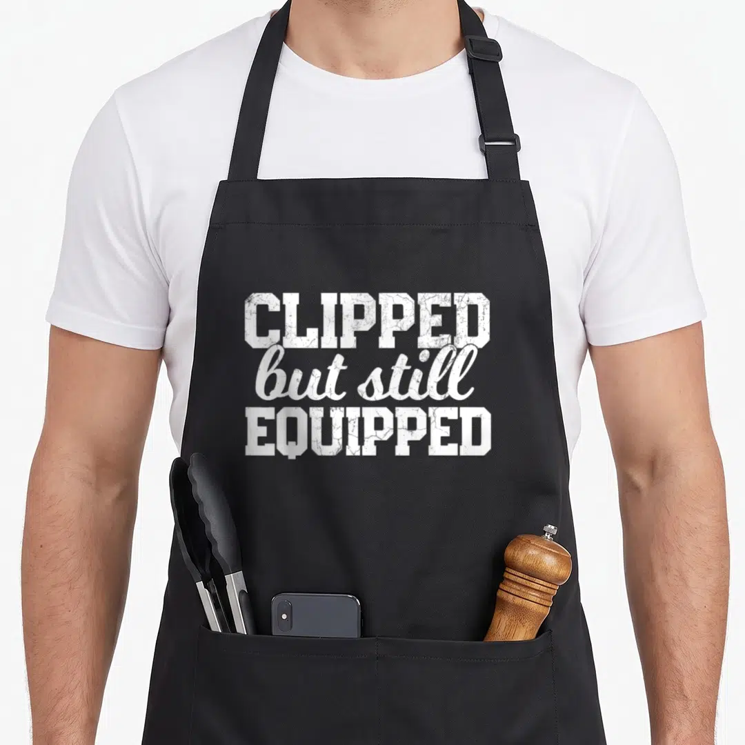 Post daddy aprons - White distressed text reading CLIPPED but still EQUIPPED stacked centrally — shown on a black cotton canvas apron against a white background
