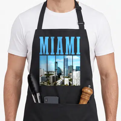 Miami skyline florida pride apron - Blue MIAMI text above a city skyline photo divided into five vertical strips — shown on a black cotton canvas apron against a white background