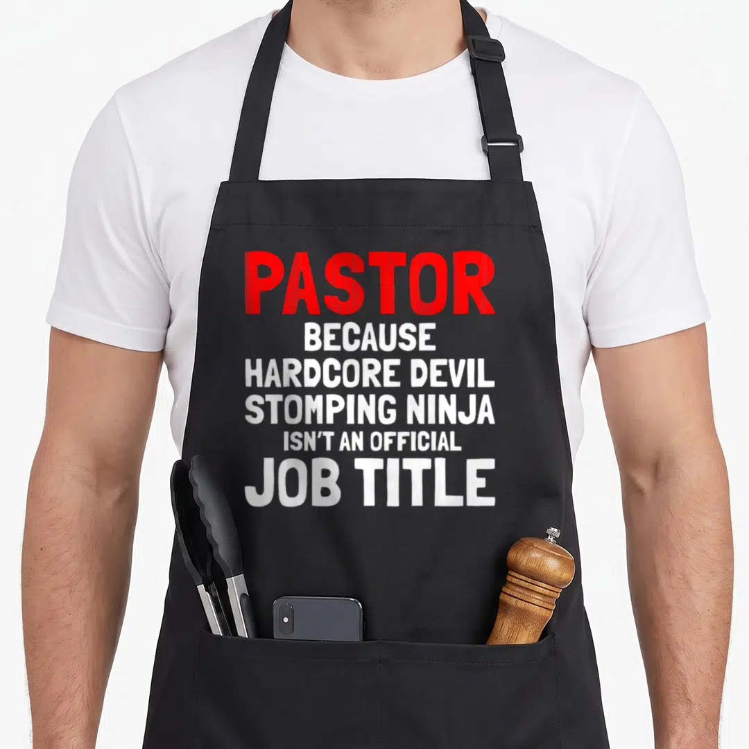 Pastor devil's apron - Red and white text reading Pastor Because Hardcore Devil Stomping Ninja Isn't An Official Job — shown on a black cotton canvas apron against a white background
