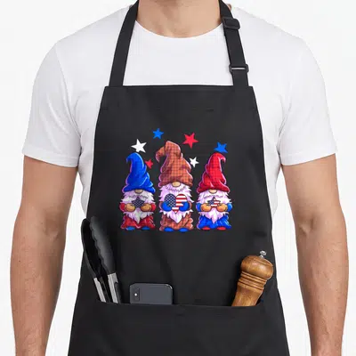 Patriotic gnome 4th of july apron - Three cartoon gnomes holding stars and a heart in red, white, and blue plaid hats — shown on a black cotton canvas apron against a white background