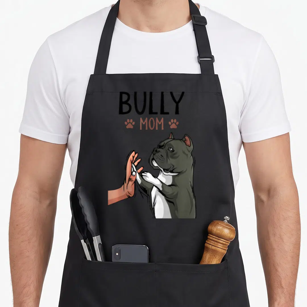 Funny bully dog apron - BULLY MOM text above a grey dog high-fiving a peach-colored hand with two paw prints — shown on a black cotton canvas apron against a white background