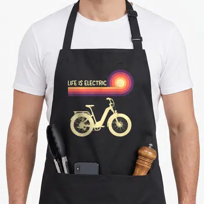 Electric ebike bike apron - LIFE IS ELECTRIC text above cream e-bike with retro sun rays in purple orange yellow — shown on a black cotton canvas apron against a white background