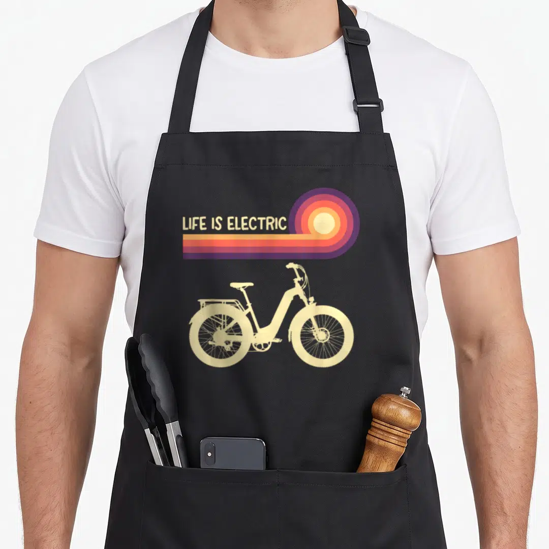 Electric ebike bike apron - LIFE IS ELECTRIC text above cream e-bike with retro sun rays in purple orange yellow — shown on a black cotton canvas apron against a white background