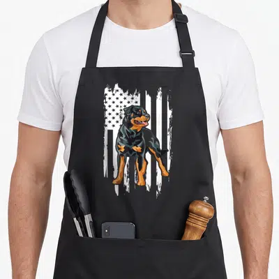 Rottweiler american flag apron - Black and tan Rottweiler standing in front of a white distressed American flag graphic — shown on a black cotton canvas apron against a white background