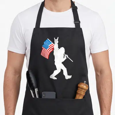 Roll bigfoot apron - White Bigfoot silhouette holding US flag and making rock-on sign — shown on a black cotton canvas apron against a white background