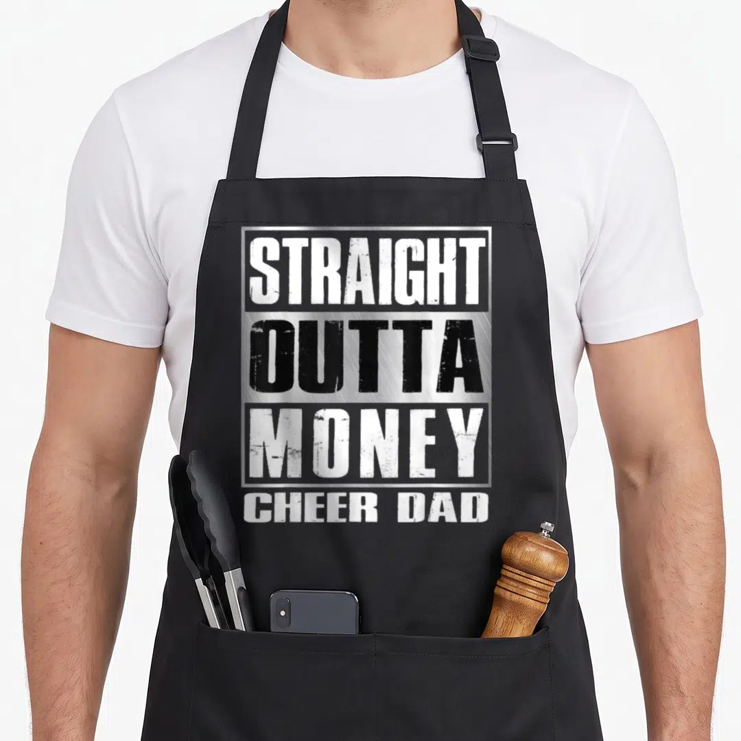 Cheer straight money apron - Stacked white and black text reading STRAIGHT OUTTA MONEY CHEER DAD inside a silver — shown on a black cotton canvas apron against a white background