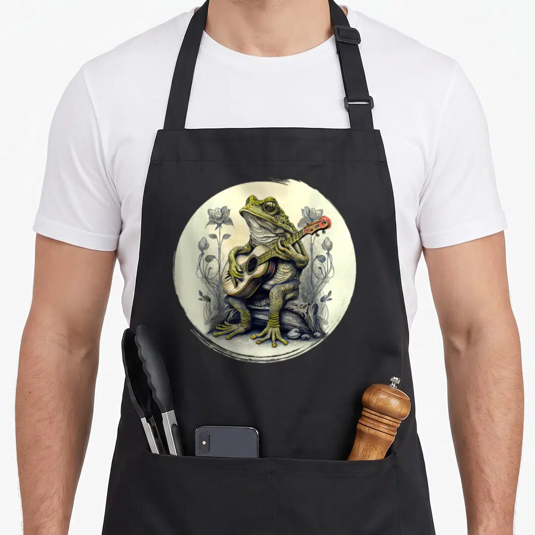 Guitar cottagecore apron - Realistic frog playing acoustic guitar surrounded by stylized flowers in green and yellow — shown on a black cotton canvas apron against a white background
