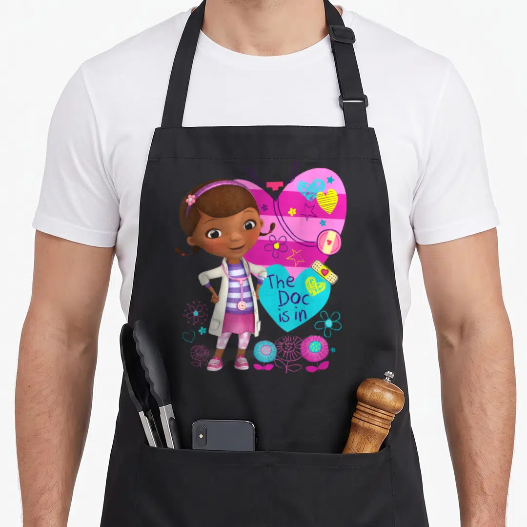 Doc dog apron - Cartoon girl doctor standing in front of pink and cyan hearts with bandages and flowers — shown on a black cotton canvas apron against a white background