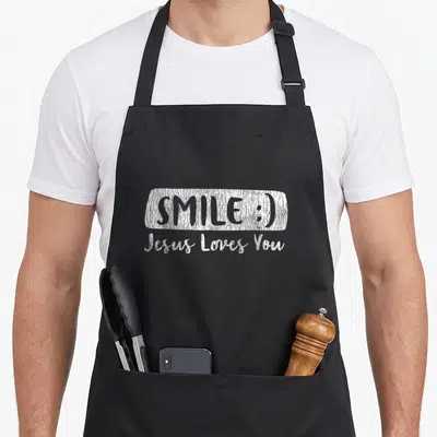 Smile christian aprons - White distressed text SMILE :) and Jesus Loves You on black fabric — shown on a black cotton canvas apron against a white background