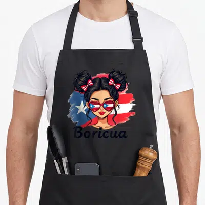 Rico messy aprons - Cartoon woman with space buns, heart sunglasses, and Boricua text over red blue white flag strokes — shown on a black cotton canvas apron against a white background