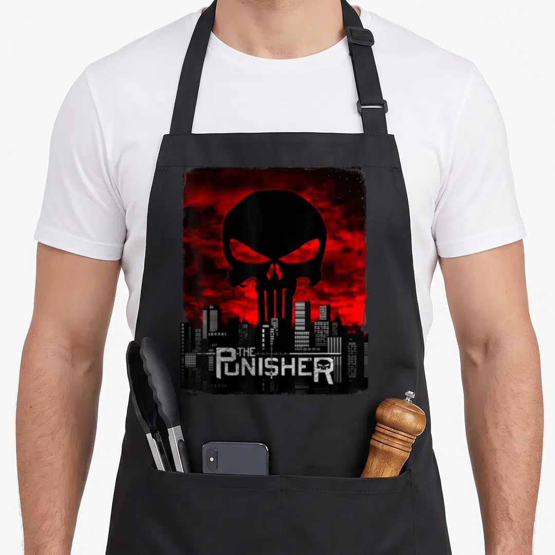 Skyline skull apron - Black skull silhouette over red cloudy sky and city skyline with THE PUNISHER text — shown on a black cotton canvas apron against a white background