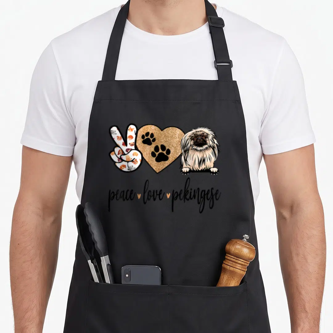 Pekingese dog apron - Peace sign with dog faces, gold glitter heart with paws, and Pekingese dog illustration — shown on a black cotton canvas apron against a white background