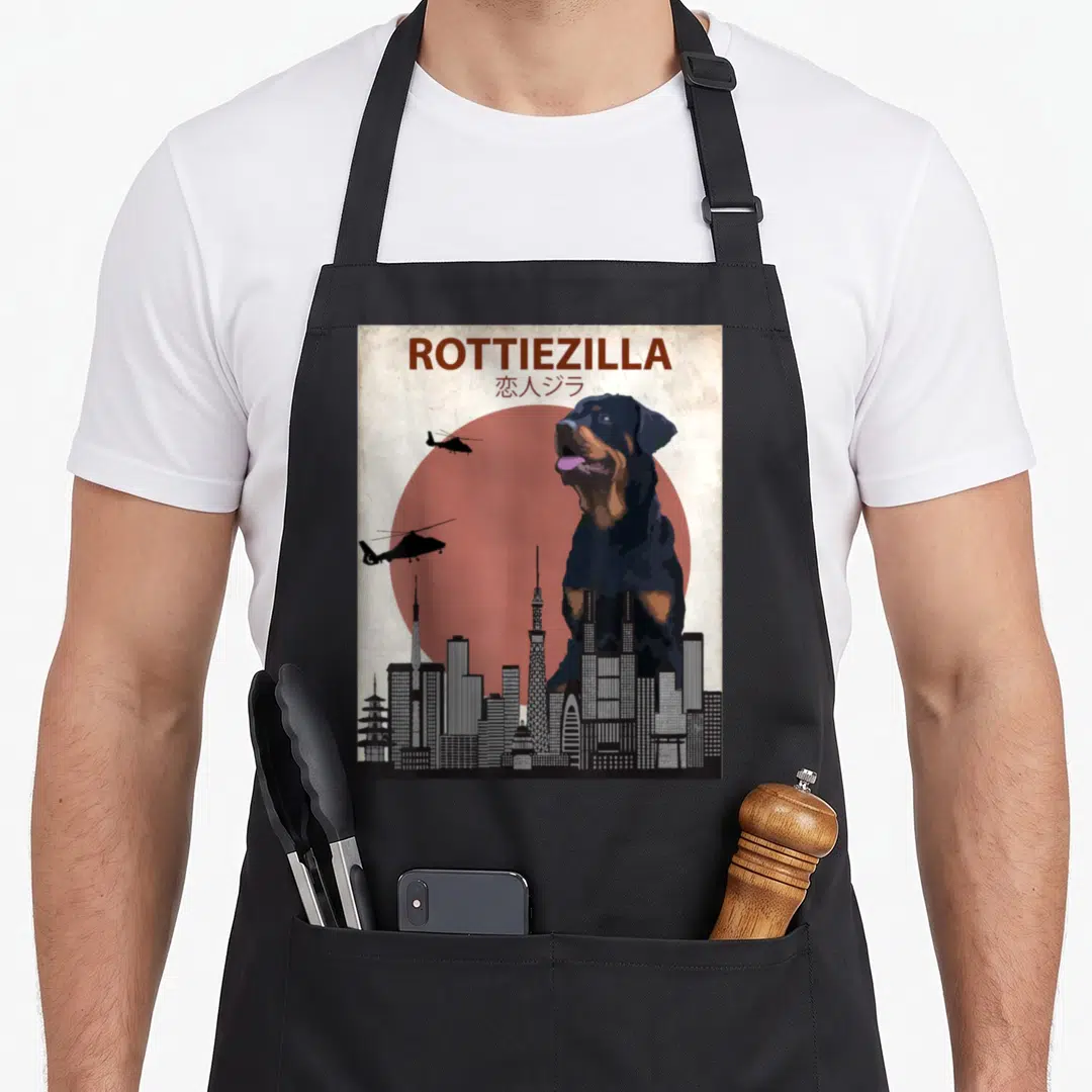 Rottweiler dog apron - Giant rottweiler dog looming over city skyline under red sun with two helicopters flying left — shown on a black cotton canvas apron against a white background