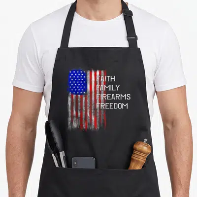 Family american flag apron - Distressed USA flag next to stacked FAITH FAMILY FIREARMS FREEDOM text in red white blue — shown on a black cotton canvas apron against a white background