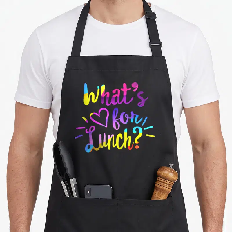 Crew cafeteria aprons - Stacked colorful text reading What's for Lunch with heart and decorative lines — shown on a black cotton canvas apron against a white background