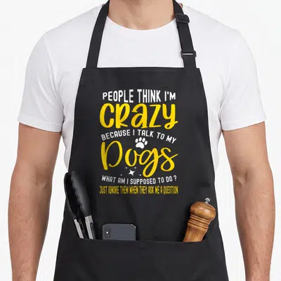 Suppose cooking with dog apron - Stacked text reading People Think I'm Crazy Because I Talk To My Dogs with paw print — shown on a black cotton canvas apron against a white background