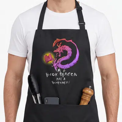 Bookish dragon apron - Purple dragon curled around glowing book with white text I'M A BOOK DRAGON NOT A BOOKWORM — shown on a black cotton canvas apron against a white background