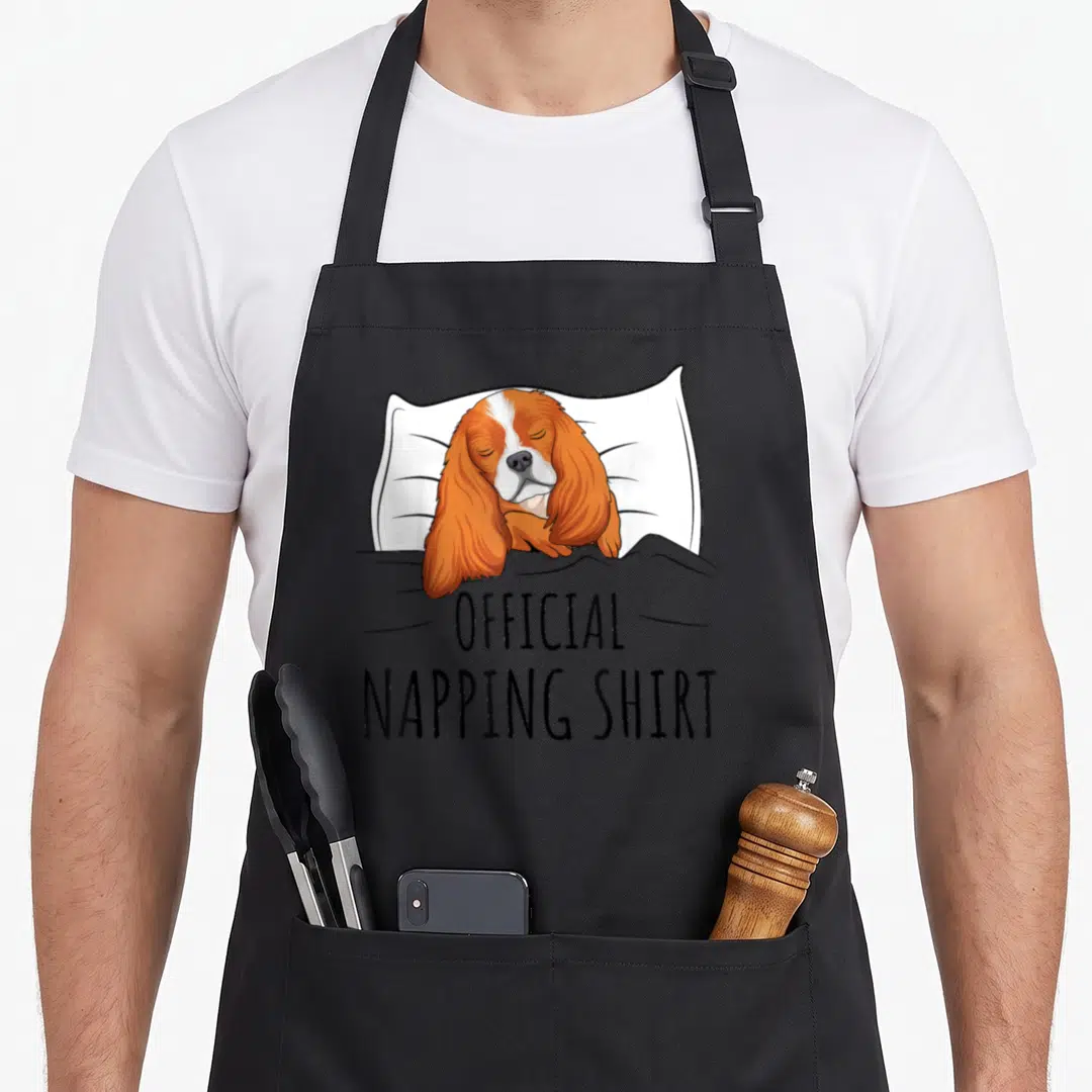 Sleeping king apron - Cartoon orange and white dog sleeping on pillow with Official Napping Shirt text — shown on a black cotton canvas apron against a white background