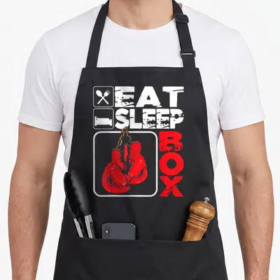 Eat box apron - Red boxing gloves on chain with white EAT SLEEP and vertical red BOX text — shown on a black cotton canvas apron against a white background