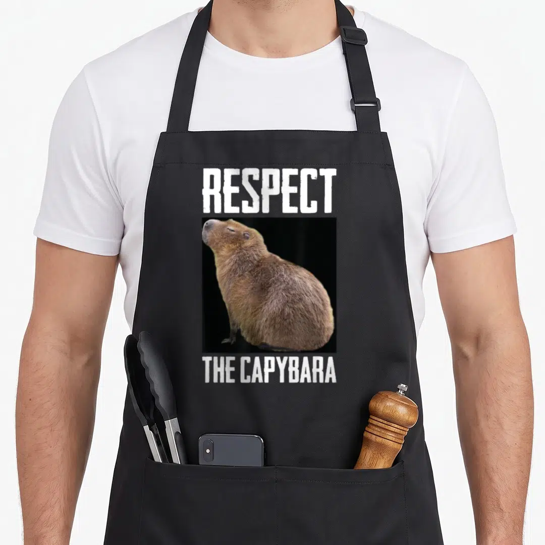 Respect lady rodent apron - White text Respect The Capybara above and below square brown rodent photo — shown on a black cotton canvas apron against a white background