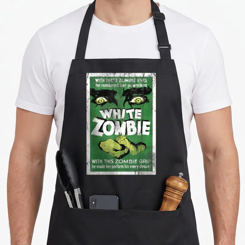 Zombie retro movie poster co apron - Green vintage poster with yellow zombie eyes, white text, and gripping hands — shown on a black cotton canvas apron against a white background