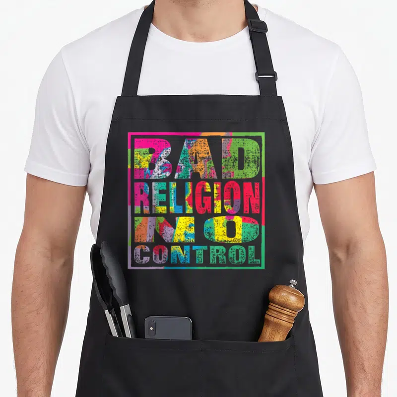 Religion control apron - Stacked BAD RELIGION IN GOD CONTROL text in pink yellow blue green red distressed block letters — shown on a black cotton canvas apron against a white background