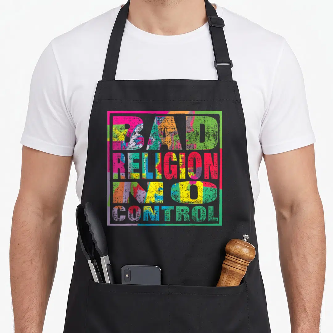 Religion control apron - Stacked BAD RELIGION IN GOD CONTROL text in pink yellow blue green red distressed block letters — shown on a black cotton canvas apron against a white background