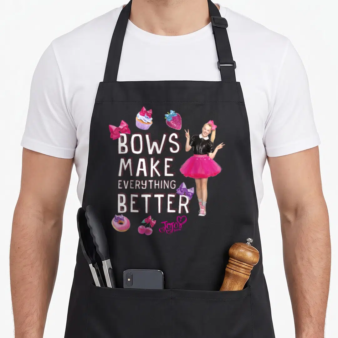 Better bow apron - BOWS MAKE EVERYTHING BETTER text with sweets and girl in pink, white, purple, red — shown on a black cotton canvas apron against a white background
