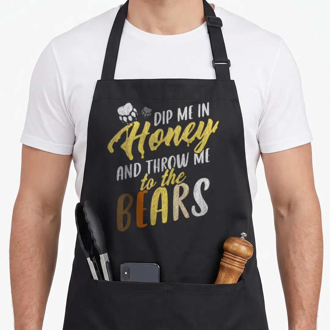 Community flag gay pride apron - Stacked text reading Dip Me In Honey And Throw Me To The Bears with a paw print — shown on a black cotton canvas apron against a white background