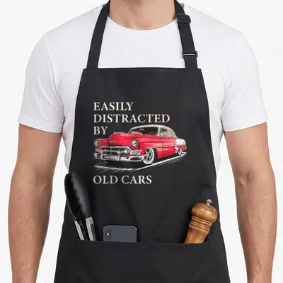 Vintage easily car apron - Red classic car illustration with EASILY DISTRACTED BY OLD CARS text — shown on a black cotton canvas apron against a white background