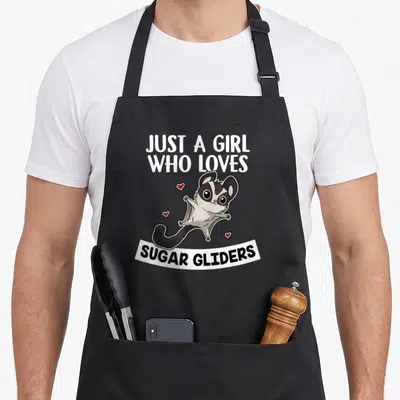 Glider sugar apron - Cartoon sugar glider with red hearts and text JUST A GIRL WHO LOVES SUGAR GLIDERS — shown on a black cotton canvas apron against a white background