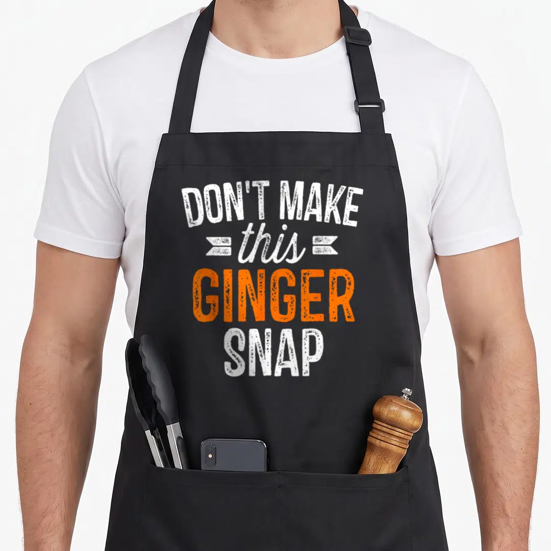 Redhead snap aprons - White and orange stacked text reading DON'T MAKE this GINGER SNAP with decorative banners — shown on a black cotton canvas apron against a white background
