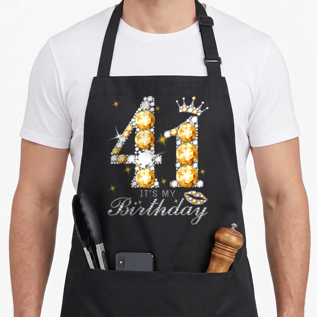 41th queen of baking apron - Jeweled number 41 with crown and IT'S MY Birthday text in gold and white crystals — shown on a black cotton canvas apron against a white background