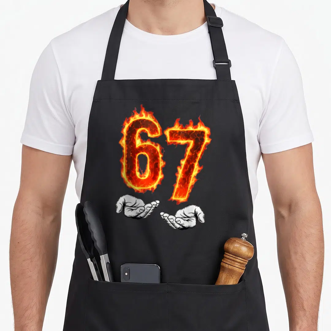 Hand meme apron - Flaming number 67 held by two open white cartoon hands in red and orange — shown on a black cotton canvas apron against a white background