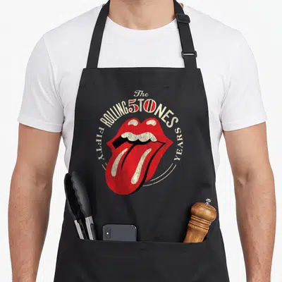 Anniversary rolling stones apron - Red mouth with tongue out surrounded by FIFTY YEARS text in retro style — shown on a black cotton canvas apron against a white background