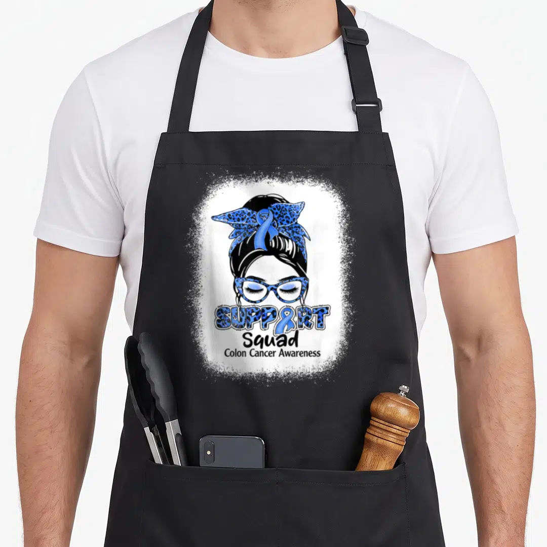 Colon messy aprons - Cartoon woman with blue leopard glasses and ribbon text reading Support Squad Colon Cancer — shown on a black cotton canvas apron against a white background