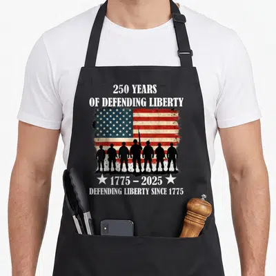 Parade patriotic apron - Seven black soldier silhouettes against distressed red white blue flag with 250 years — shown on a black cotton canvas apron against a white background