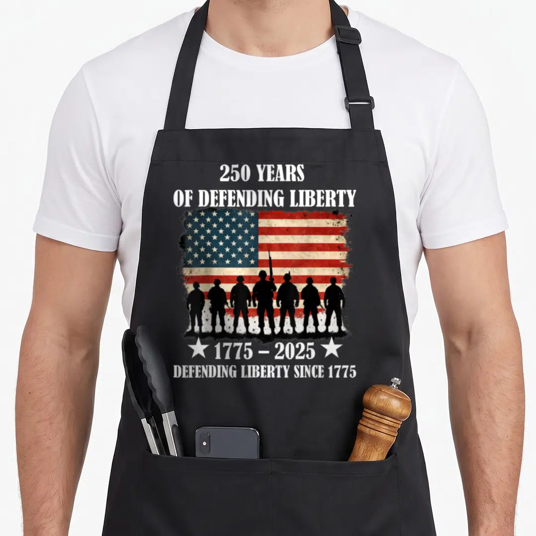 Parade patriotic apron - Seven black soldier silhouettes against distressed red white blue flag with 250 years — shown on a black cotton canvas apron against a white background