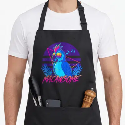 Macawsome 80s apron - Blue macaw in sunglasses surrounded by purple circle, pink triangle, music notes, and palm leaves — shown on a black cotton canvas apron against a white background