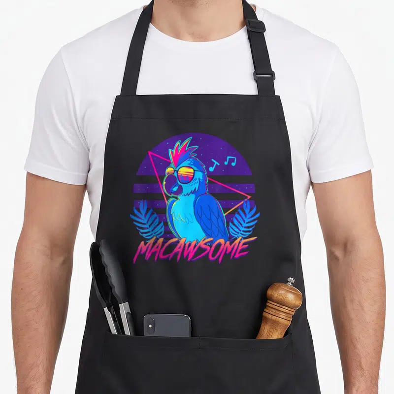 Macawsome 80s apron - Blue macaw in sunglasses surrounded by purple circle, pink triangle, music notes, and palm leaves — shown on a black cotton canvas apron against a white background