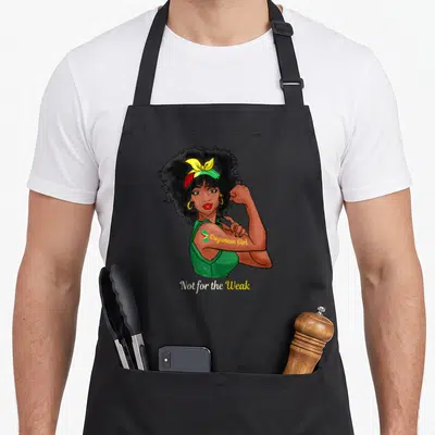 Weak guyana apron - Cartoon woman flexing arm with Guyanese Girl tattoo and Not for the Weak text — shown on a black cotton canvas apron against a white background