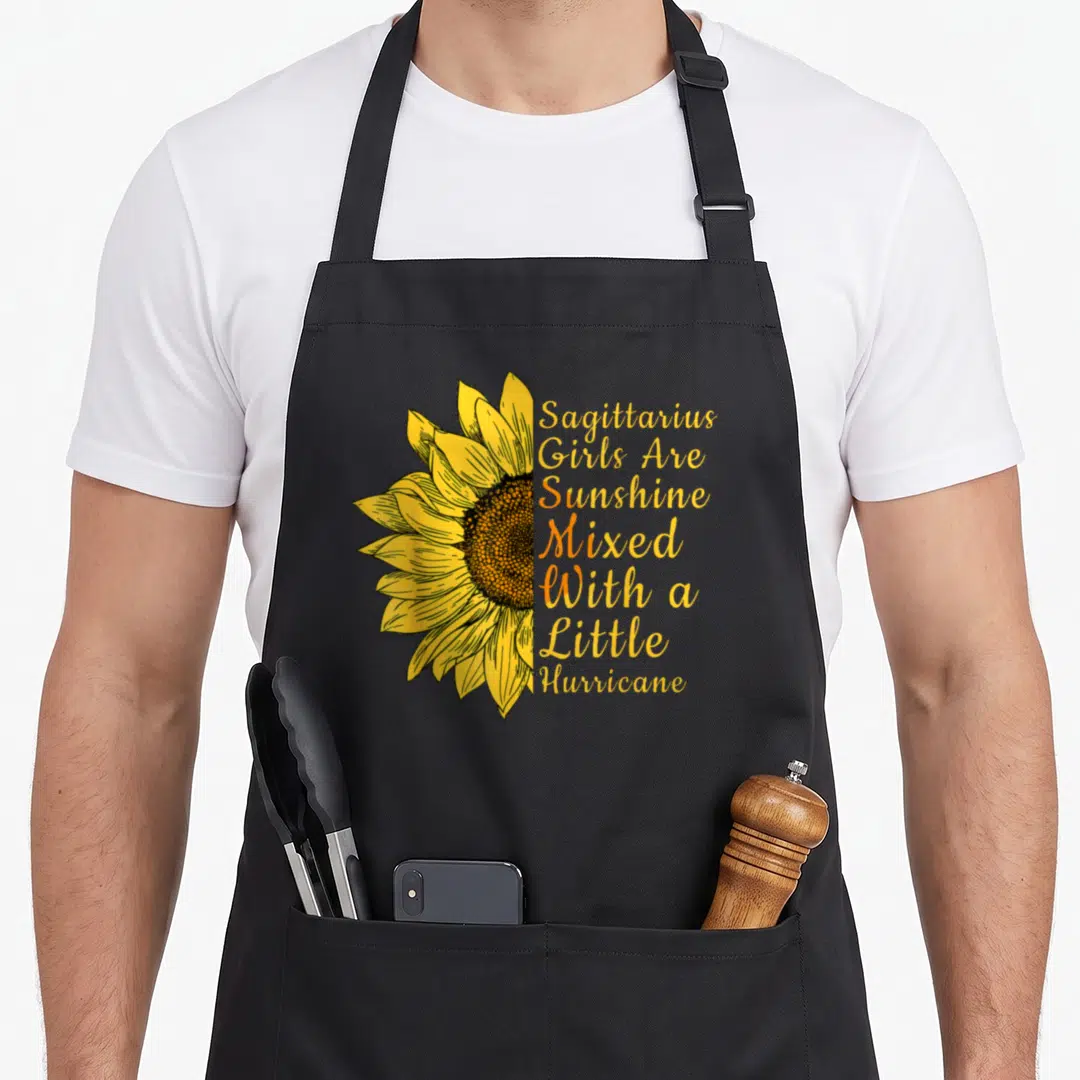 Sagittarius sunflower apron - Half yellow sunflower next to stacked text Sagittarius Girls Are Sunshine Mixed — shown on a black cotton canvas apron against a white background