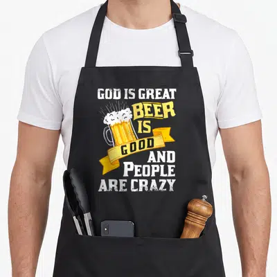 Funny god beer apron - Retro mug with yellow ribbon and text 'GOD IS GREAT BEER IS GOOD AND PEOPLE ARE CRAZY' in white — shown on a black cotton canvas apron against a white background