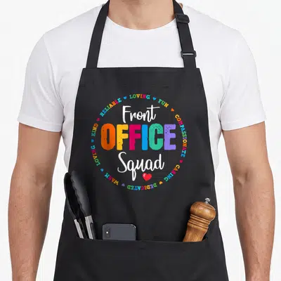 School office apron - Colorful Front Office Squad text surrounded by adjectives and hearts on black fabric — shown on a black cotton canvas apron against a white background