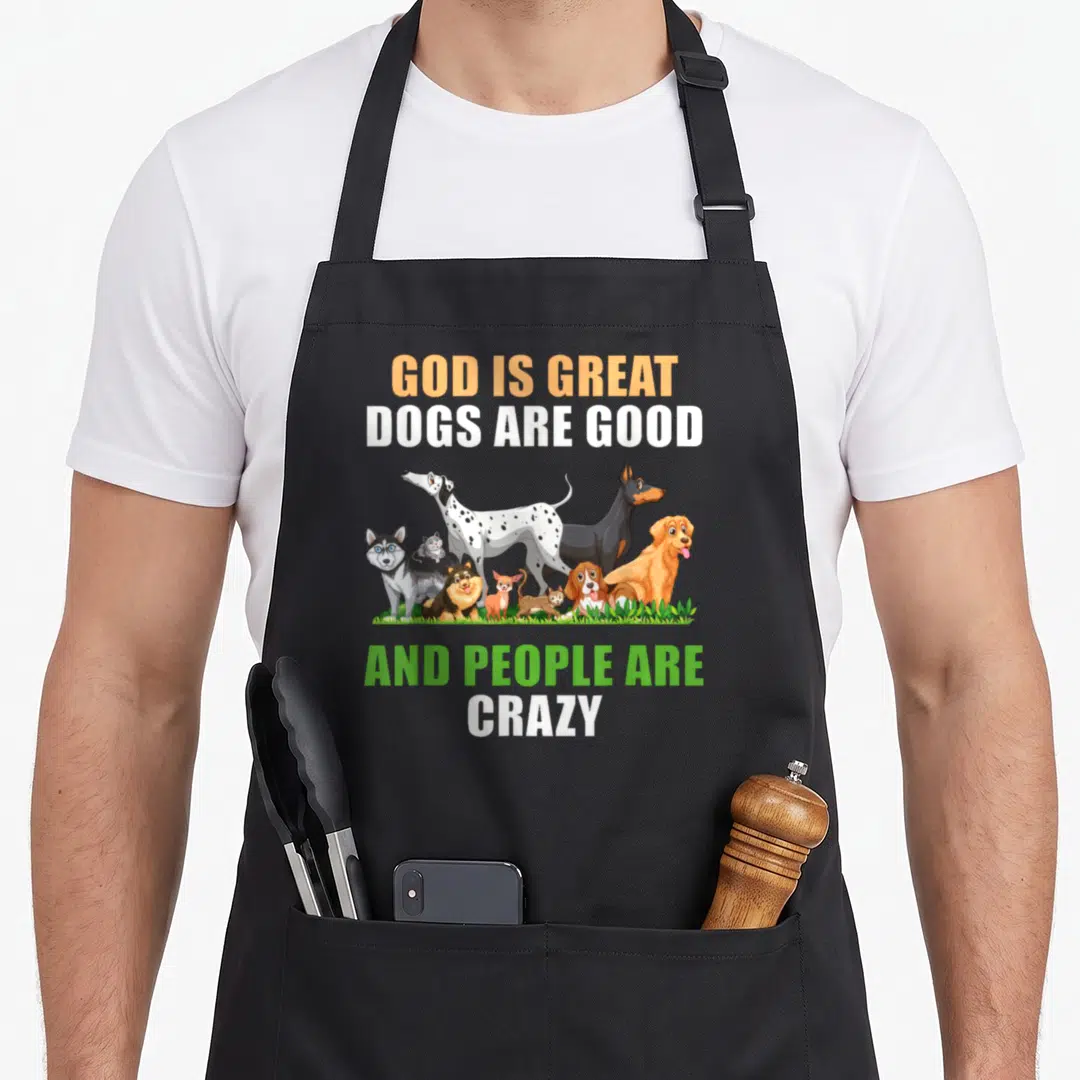 Funny god cooking with dog apron - Cartoon dogs on grass with text GOD IS GREAT DOGS ARE GOOD AND PEOPLE ARE CRAZY — shown on a black cotton canvas apron against a white background